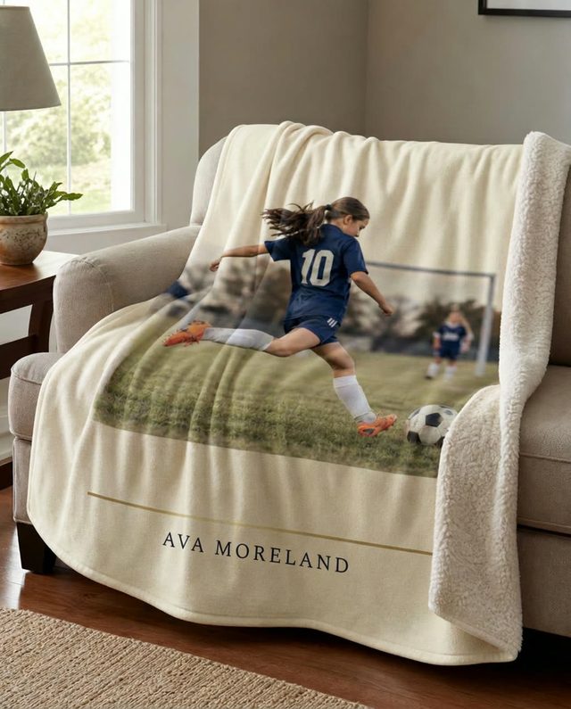 A GameYears sherpa blanket printed with a youth soccer photograph, draped over a family-room sofa