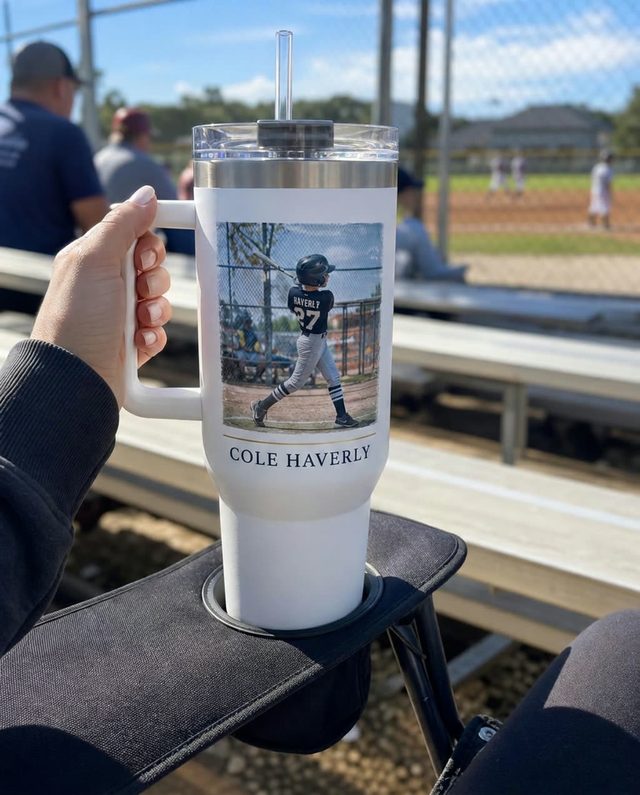 A parent holding a 40 oz GameYears tumbler in the bleachers at a youth baseball game